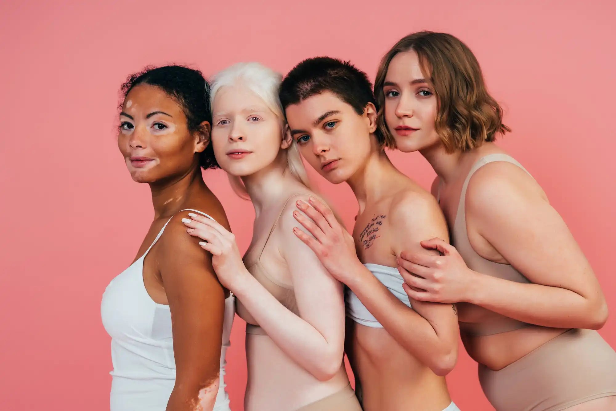 Groupe de quatre femmes diverses posant ensemble contre un fond rose.